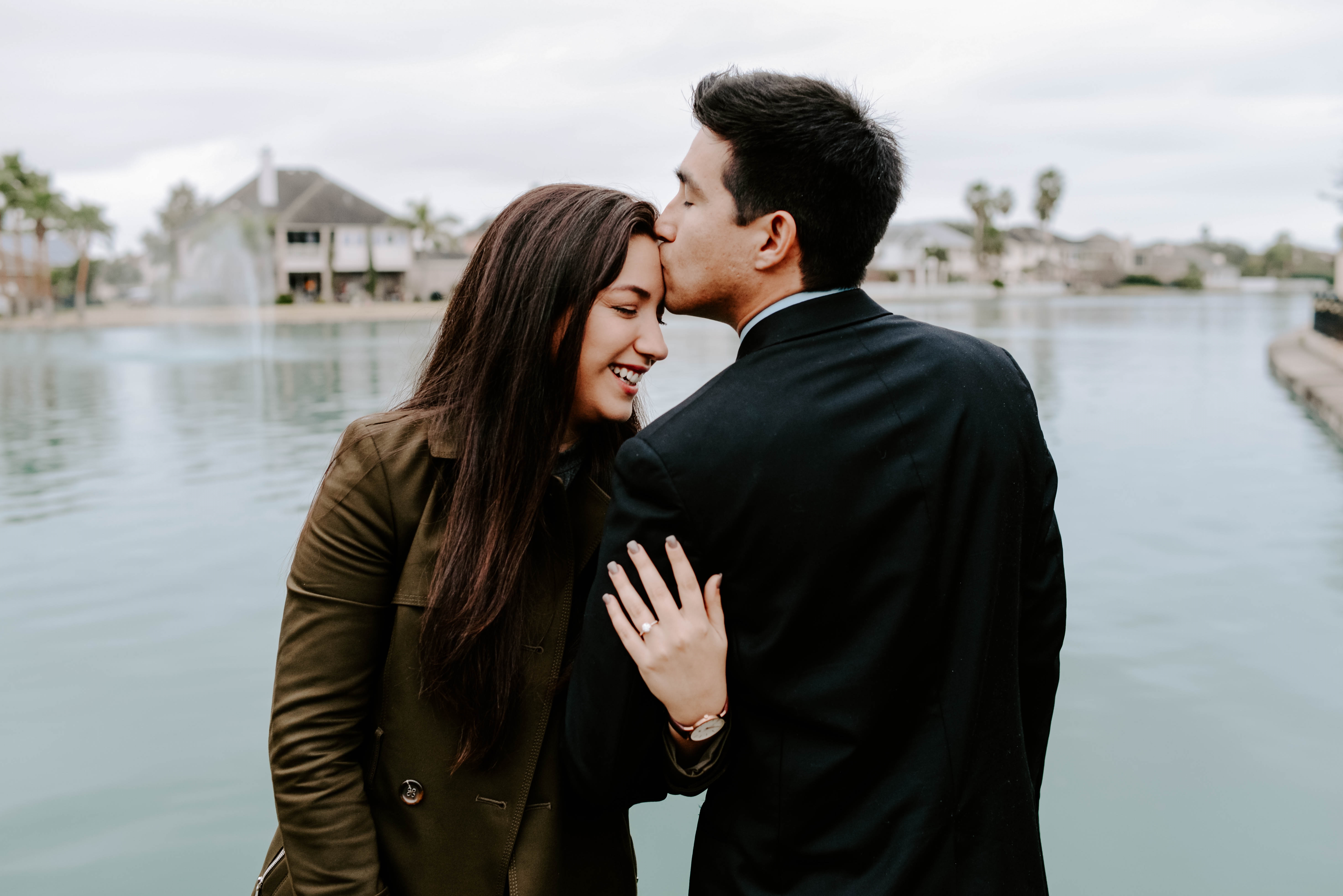 Couple by a lakeside sharing a romantic moment, with the woman wearing a diamond engagement ring visible on her hand